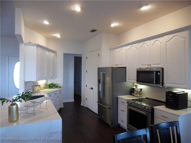 kitchen with dark wood-style floors, a sink, light stone counters, white cabinets, and appliances with stainless steel finishes
