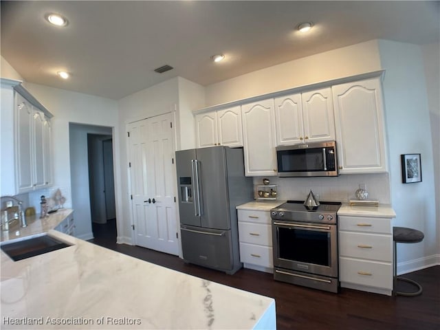 kitchen featuring white cabinets, appliances with stainless steel finishes, decorative backsplash, and a sink
