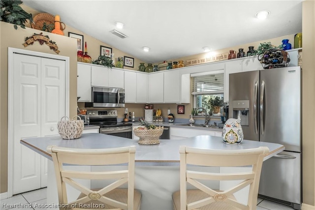 kitchen with appliances with stainless steel finishes, light tile patterned floors, white cabinetry, and lofted ceiling