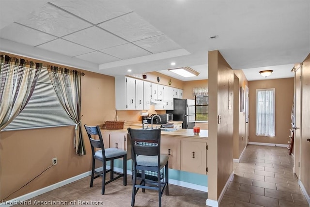 kitchen featuring black refrigerator, tile patterned floors, white cabinetry, and sink