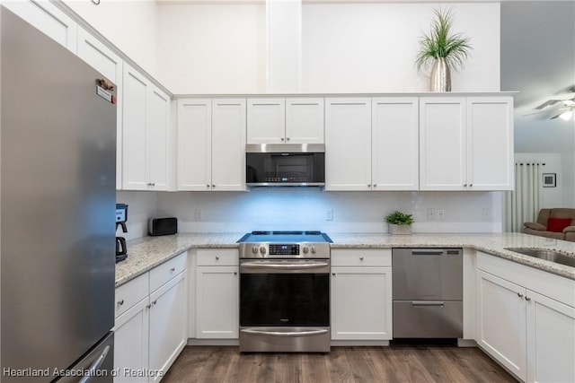 kitchen with appliances with stainless steel finishes, kitchen peninsula, light stone counters, dark hardwood / wood-style floors, and white cabinets