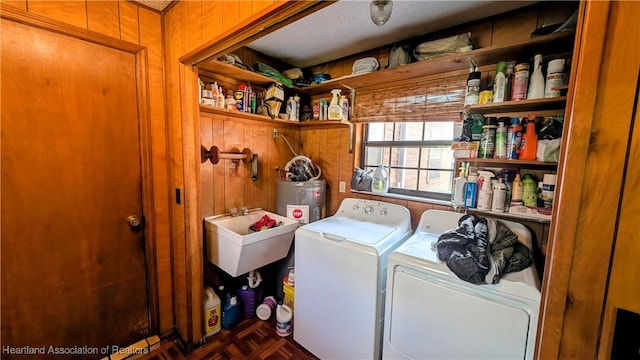 clothes washing area featuring sink, parquet floors, wooden walls, washing machine and dryer, and water heater