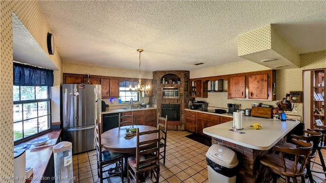 kitchen with sink, a chandelier, hanging light fixtures, black appliances, and wall chimney range hood