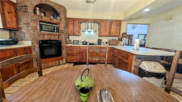 kitchen featuring stainless steel microwave, black oven, wall chimney exhaust hood, and light tile patterned flooring