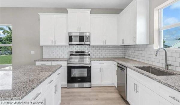 kitchen with appliances with stainless steel finishes, white cabinetry, sink, light stone counters, and a healthy amount of sunlight