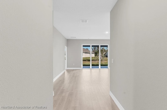 corridor with a textured ceiling and light wood-type flooring