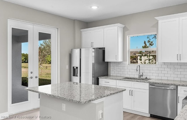 kitchen with a kitchen island, appliances with stainless steel finishes, sink, white cabinets, and light stone counters