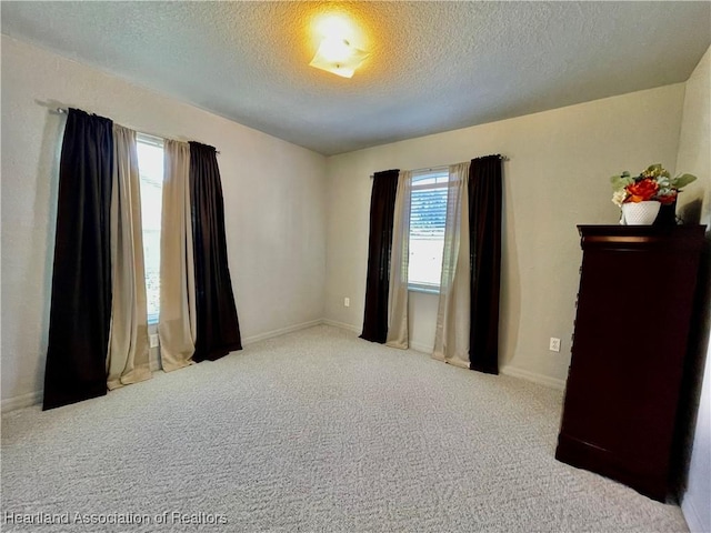 carpeted empty room with a textured ceiling and baseboards