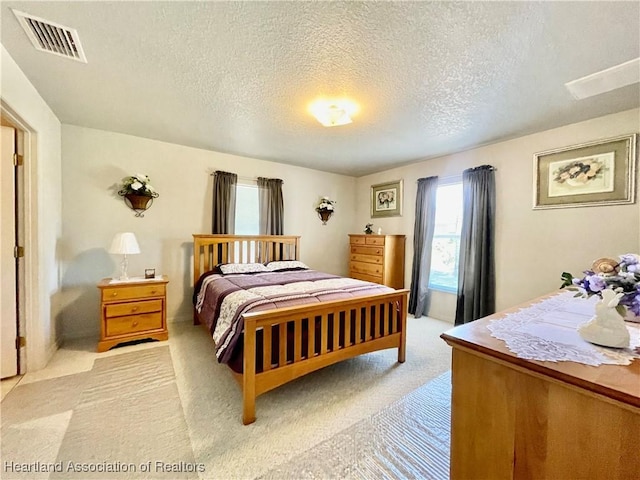 bedroom with a textured ceiling, visible vents, and light colored carpet