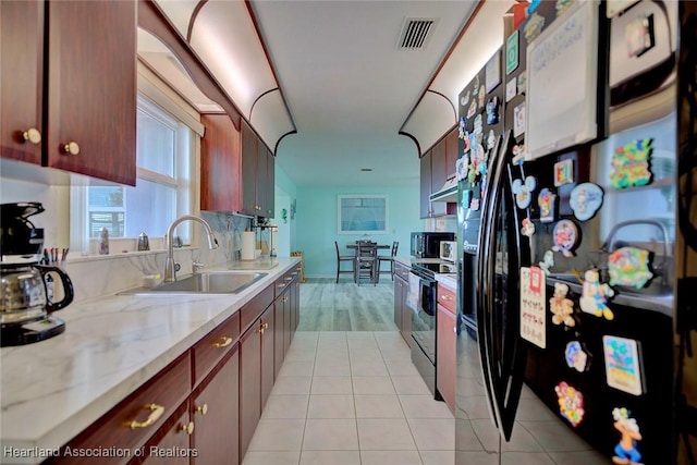 kitchen featuring light stone countertops, black fridge with ice dispenser, stainless steel electric stove, sink, and light tile patterned floors