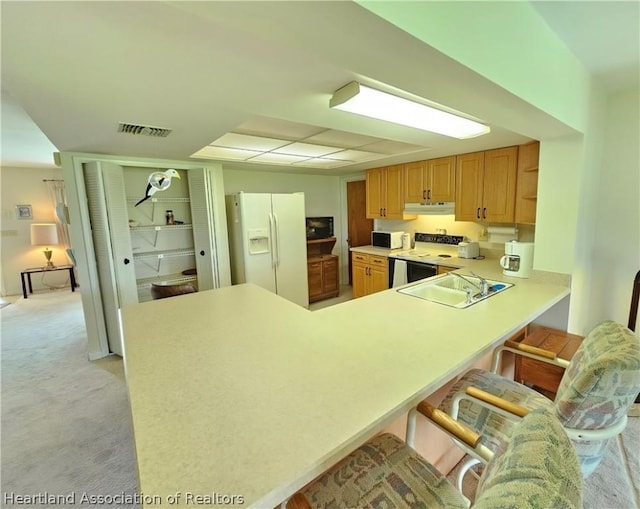 kitchen with white appliances, light carpet, a kitchen breakfast bar, sink, and kitchen peninsula