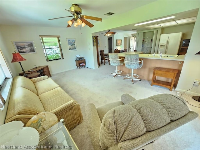 carpeted living room featuring ceiling fan and sink