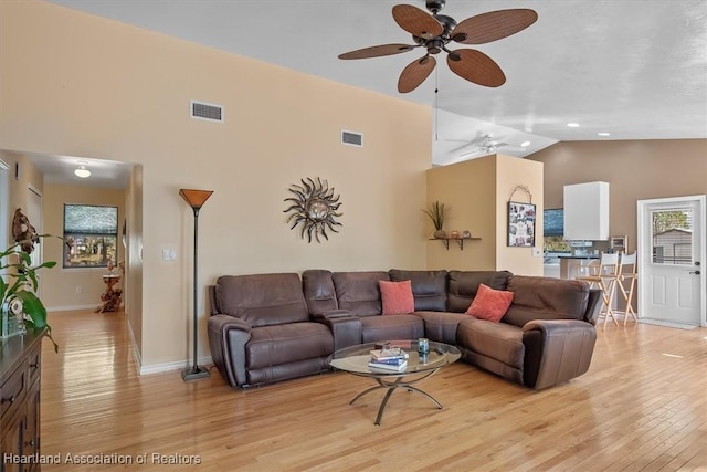 living area with ceiling fan, high vaulted ceiling, light wood-style flooring, visible vents, and baseboards