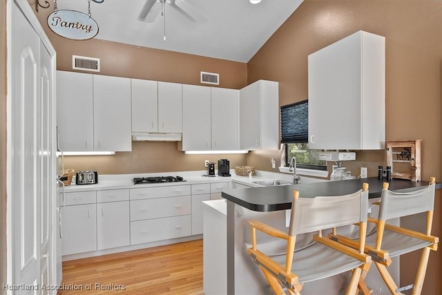 kitchen featuring black gas cooktop, visible vents, a peninsula, under cabinet range hood, and a kitchen breakfast bar