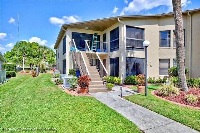 view of front of home featuring central air condition unit, stairway, a front yard, and stucco siding