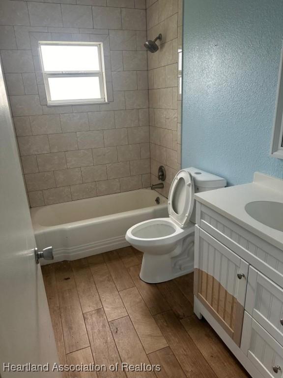 full bathroom with vanity, hardwood / wood-style floors, tiled shower / bath combo, and toilet