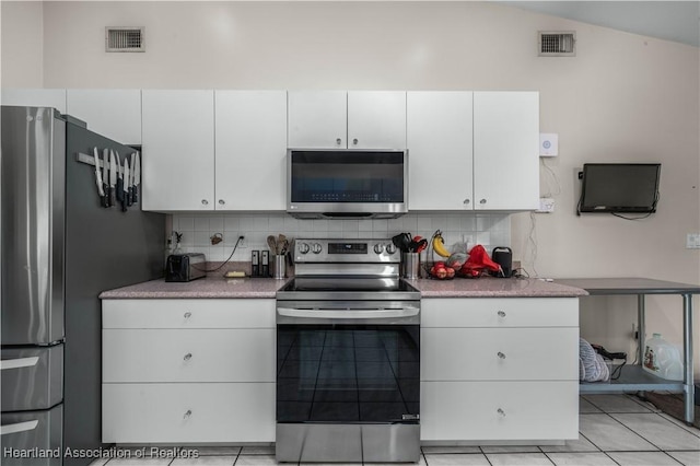 kitchen with appliances with stainless steel finishes, lofted ceiling, white cabinetry, decorative backsplash, and light tile patterned floors