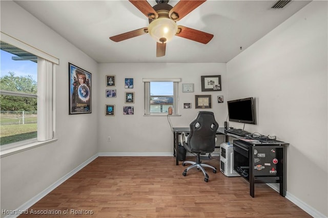 office featuring light wood-type flooring, ceiling fan, and a healthy amount of sunlight