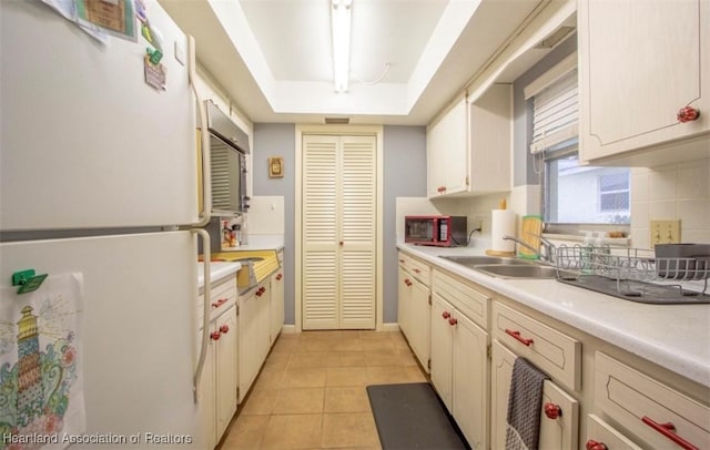 kitchen featuring backsplash, sink, a tray ceiling, light tile patterned floors, and white refrigerator