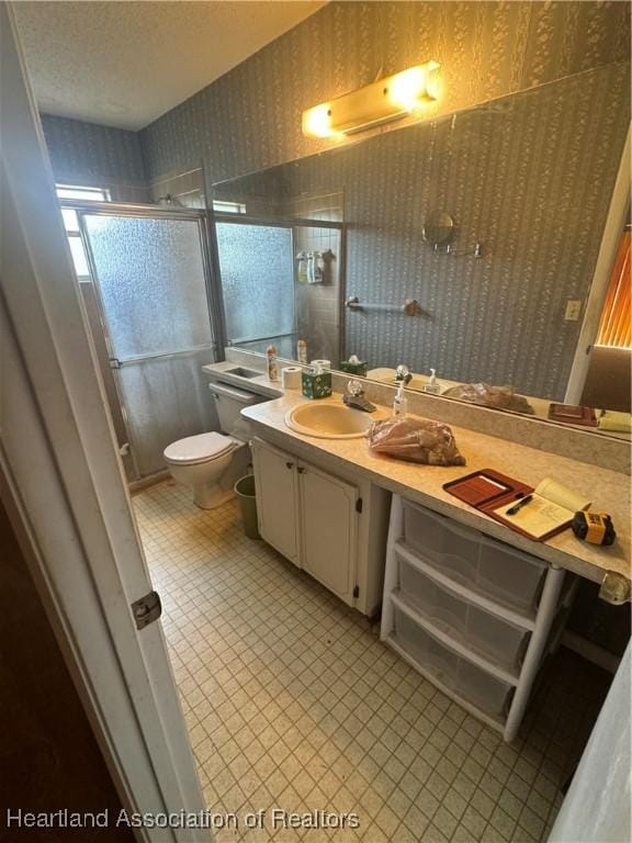 bathroom featuring a shower with door, vanity, and toilet