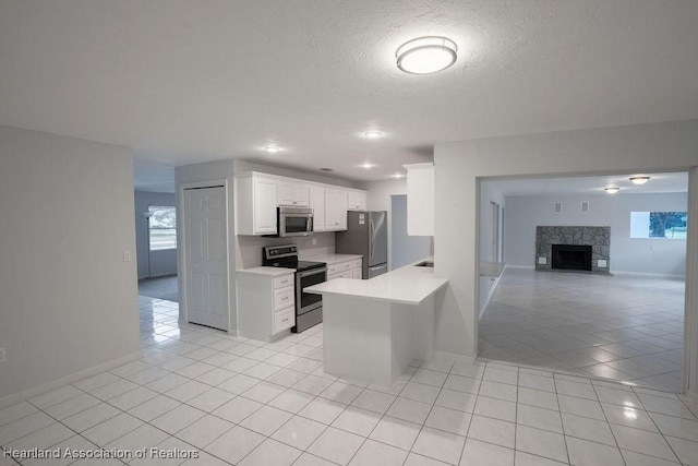 kitchen featuring white cabinetry, stainless steel appliances, a fireplace, kitchen peninsula, and light tile patterned flooring