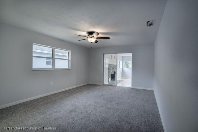 unfurnished room with ceiling fan, carpet flooring, a fireplace, and a wealth of natural light