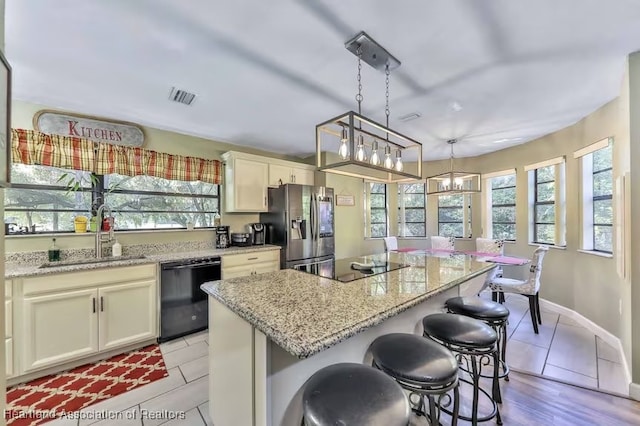 kitchen with light stone countertops, a center island, sink, hanging light fixtures, and black appliances