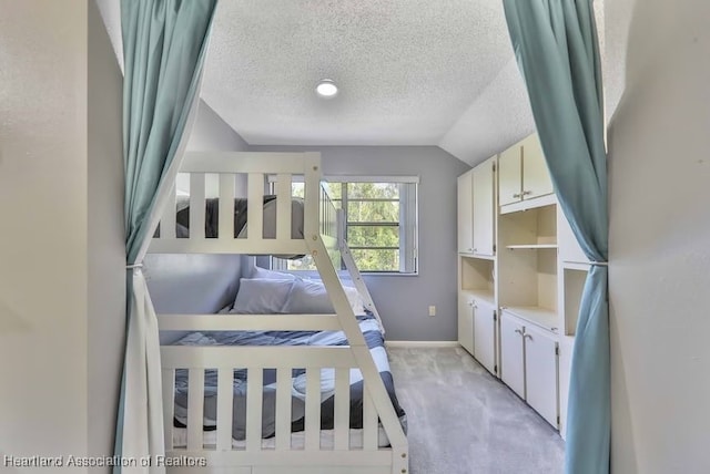 bedroom with lofted ceiling, a textured ceiling, and light carpet