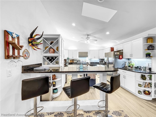 kitchen featuring lofted ceiling with skylight, kitchen peninsula, ceiling fan, white cabinetry, and a breakfast bar area