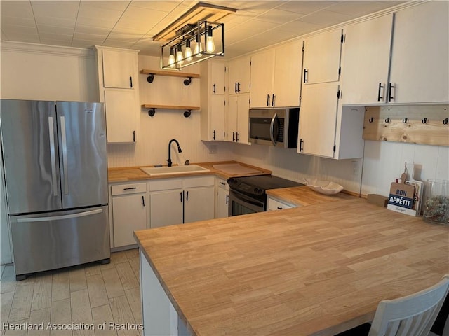 kitchen featuring a peninsula, open shelves, a sink, hanging light fixtures, and stainless steel appliances