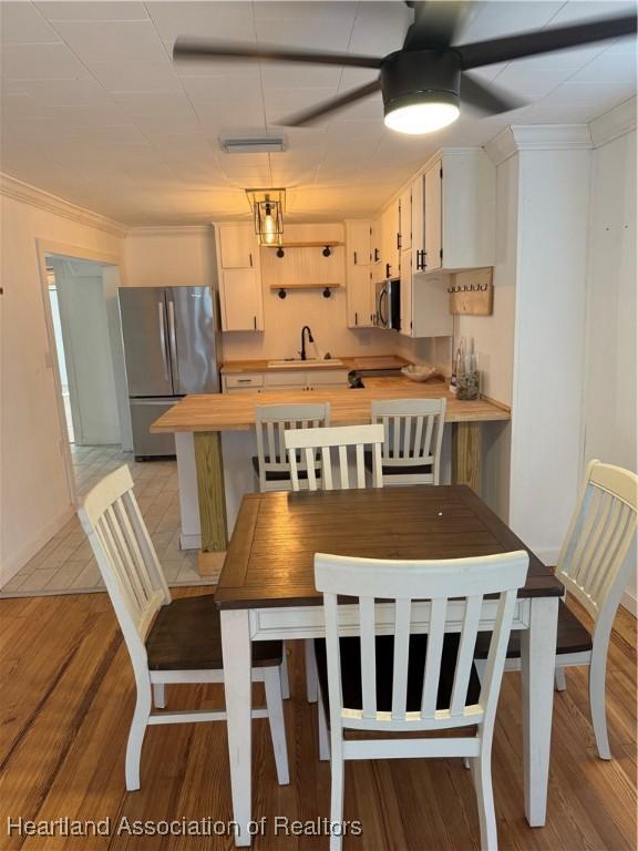dining room featuring light wood-type flooring, baseboards, ornamental molding, and ceiling fan