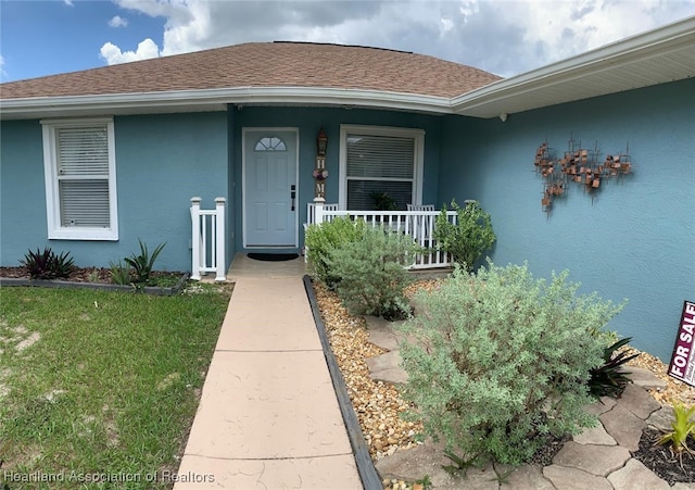 2010 W Royalton Rd, Avon Park, FL 33825 - view of exterior entry with stucco siding, covered porch, a shingled roof, and a lawn