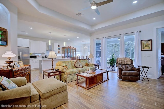 living room featuring ceiling fan, a tray ceiling, and light hardwood / wood-style flooring