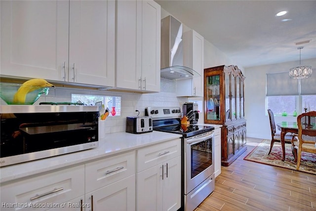 kitchen featuring white cabinetry, decorative backsplash, stainless steel appliances, light wood-type flooring, and wall chimney exhaust hood