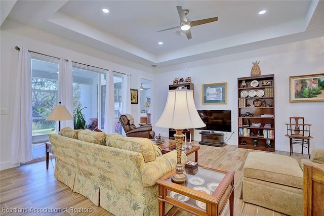 living room featuring a raised ceiling, ceiling fan, and light hardwood / wood-style flooring