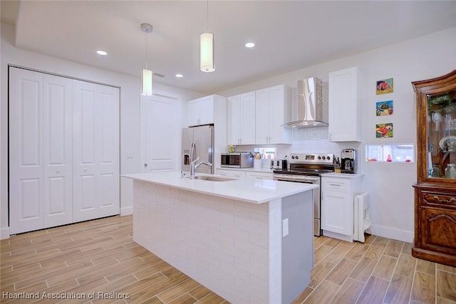 kitchen featuring wall chimney exhaust hood, sink, decorative light fixtures, stainless steel appliances, and white cabinets