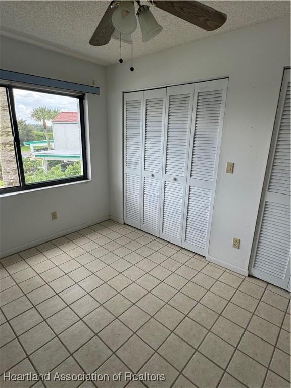 unfurnished bedroom featuring ceiling fan, a closet, light tile patterned floors, and a textured ceiling