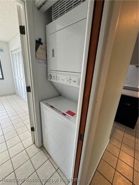 laundry room featuring stacked washing maching and dryer, a textured ceiling, and light tile patterned floors