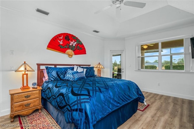 bedroom featuring a raised ceiling, ceiling fan, crown molding, multiple windows, and hardwood / wood-style floors