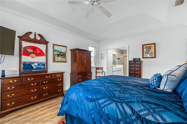 bedroom featuring light hardwood / wood-style flooring, ensuite bath, ceiling fan, ornamental molding, and a tray ceiling