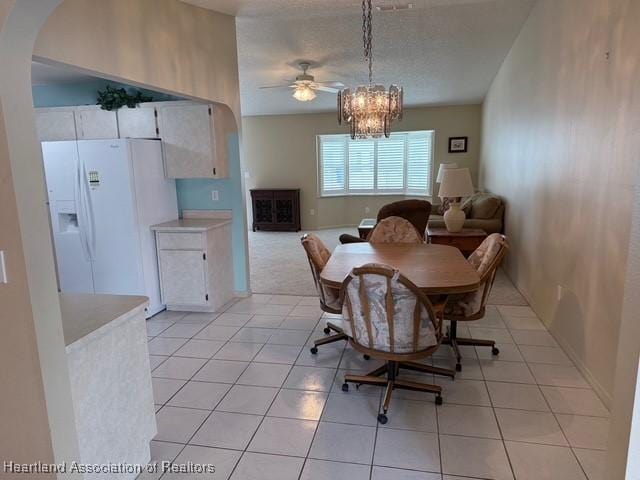 tiled dining room with ceiling fan with notable chandelier and a textured ceiling