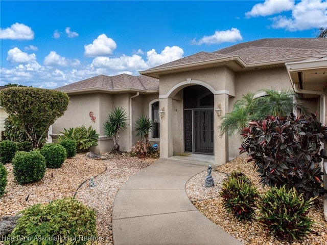 view of exterior entry with a garage, roof with shingles, and stucco siding