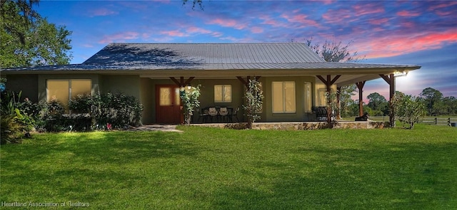 back of house featuring a yard, metal roof, a porch, and stucco siding