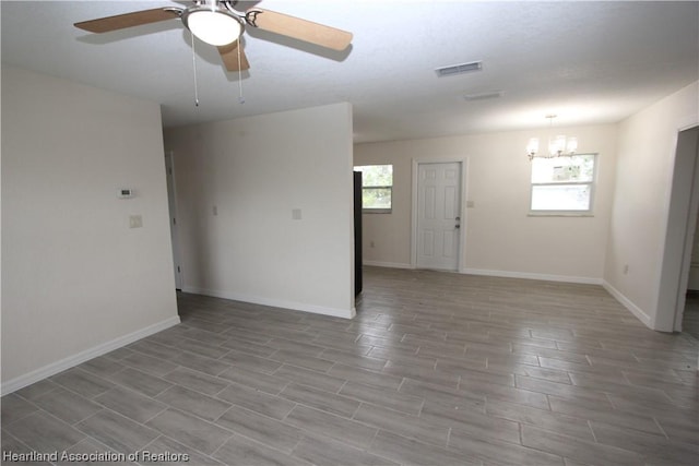 spare room featuring ceiling fan with notable chandelier