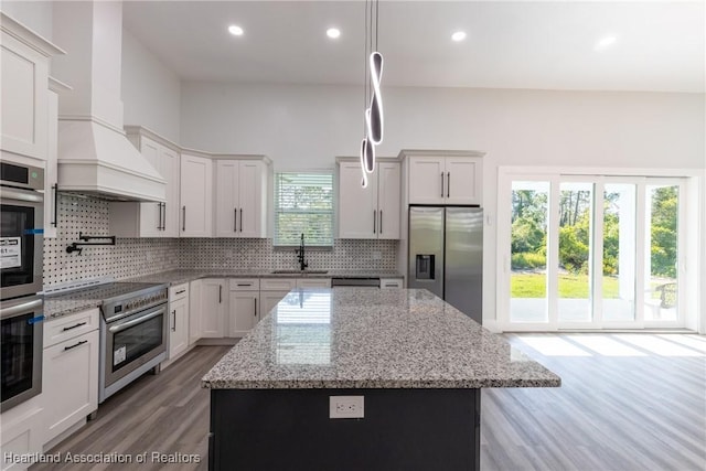 kitchen with a sink, appliances with stainless steel finishes, a center island, wood finished floors, and backsplash