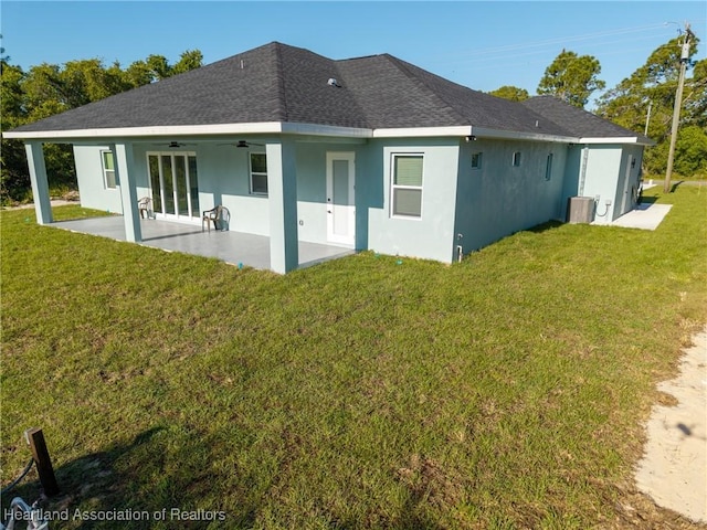 back of property featuring a patio area, a shingled roof, a ceiling fan, stucco siding, and a yard