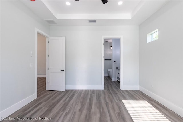 unfurnished bedroom with wood finished floors, visible vents, a tray ceiling, and baseboards