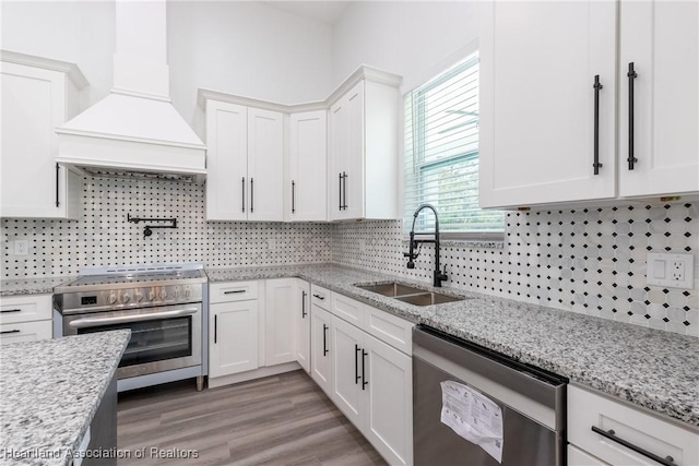 kitchen with a sink, stainless steel appliances, tasteful backsplash, white cabinetry, and premium range hood