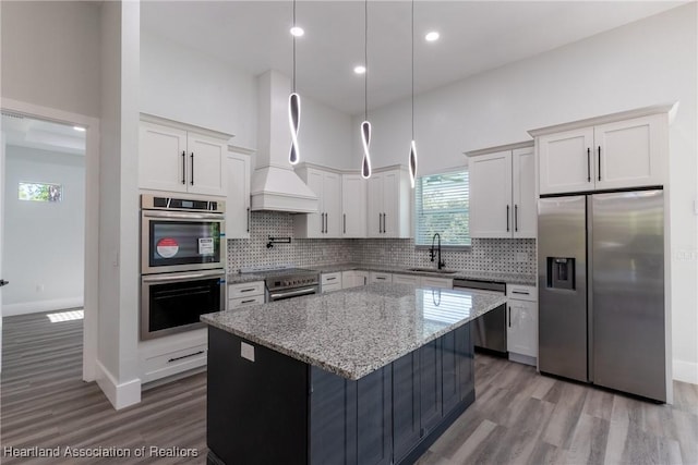 kitchen featuring appliances with stainless steel finishes, wood finished floors, a kitchen island, and a sink