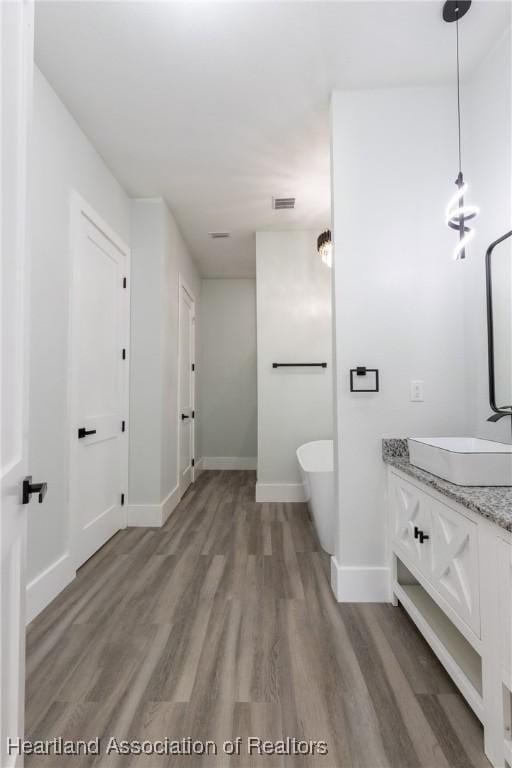 full bathroom with a soaking tub, wood finished floors, vanity, and baseboards